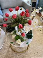 Photo of multiple faux flower and plant arrangements on a round white and gold coffee table.
