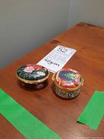 Two Halcyon Days enamel jewelry boxes on a wooden surface, one with floral design and one with Christmas design.