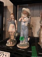 Two Lladro porcelain figurines: boy in overalls with basket, girl in dress with hat, both on floral bases.