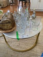 Round marble top coffee table with brass base, placed on woven beige rug with various glass decorative items on top.
