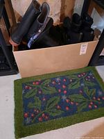 Photo of the sisal doormat showing a blue background with green leaf and red berry design, placed on the floor near a box with footwear.