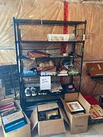 Front view of the black metal 5-shelf rack loaded with miscellaneous items to illustrate shelves and condition.