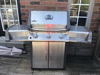 Front view of grill showing three control knobs, integrated lid thermometer, Napoleon logo, side shelves and cabinet doors.