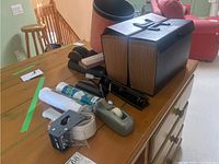 View of the lot on a wooden table showing an accordion file folder, staplers, tape dispenser, paper rolls, and waste paper bin