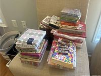 Multiple stacks of assorted paper napkins in various colors and patterns, some packaged, placed on and next to a chair and couch.