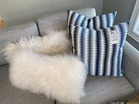 View of both pairs of pillows: a pair of fluffy white cushions and a pair of blue, white, and black striped patterned cushions, positioned on a light grey couch.