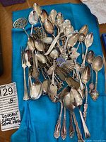 Various spoons laid out on blue cloth displaying diversity in size, shape, design, and condition.