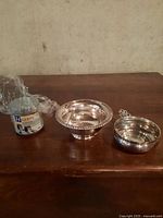 Birks sterling bowl, silver plate bowl with handle, and Hagerty silver foam cleaner container on wooden surface.