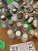 Front and top view of nine glass salt and pepper shakers with sterling silver lids on table, showing varying cut glass patterns and lid styles.
