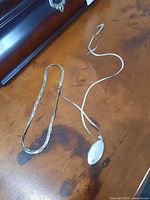 Photo of sterling silver bracelet and silver necklace with locket on wooden surface.