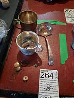 Overhead shot showing two silver cups, ladle, ring, pin and necklace