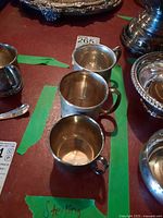 Overhead view of three sterling silver cups on table surrounded by other items