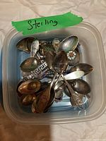 Plastic container labeled 'Sterling' holding piled decorative spoons