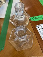 Pair of clear crystal candle holders with hexagonal bases placed on a wooden surface, showing faceted cylindrical tops designed to hold candles.