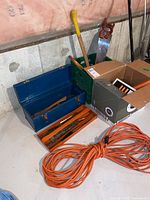 Photo of blue metal toolbox and orange extension cord with a crate and large saws in the background