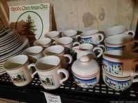 Overview of nine small mugs front left, four large mugs right, sugar bowl and creamer in center on metal shelf.