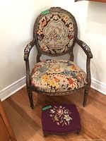 Front view of vintage tapestry upholstered armchair with matching footstool in corner.