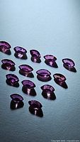 Fourteen marquis cut rubies in various red, pink, purple shades arranged on a light surface showing brilliance and clarity.