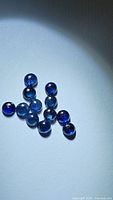 Photo showing a loose lot of twelve natural round blue sapphire cabochons with smooth surfaces under focused light to highlight color and clarity.