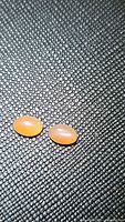 Two oval peach colored catseye moonstones placed on a black textured background, showing their cabochon shape and silky chatoyancy.