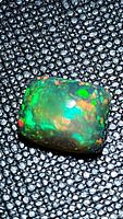 Close-up image of a cushion cabochon cut natural Ethiopian black opal with intense rainbow play of color, vibrant green dominant with red and orange accents.
