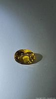 Oval-cut golden yellow Helidor gemstone with natural facets and high clarity, displayed on a white surface with light shadow to highlight facets.