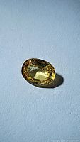 Close-up photo showing an oval-cut natural yellow sapphire on a blue background with visible facets and brilliance.