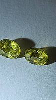 Two oval cut yellow-green sphene gemstones shown side by side on a blank surface, showcasing their color and faceting.