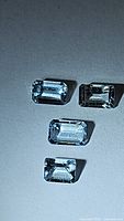 Four emerald cut aquamarine gemstones placed on a flat surface with a plain background, showing clarity and cut of each stone.