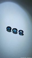 Three oval cut blue sapphire gemstones displayed on a white surface, showing deep blue color and faceting.