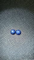 Pair of round blue star sapphire cabochons with visible star effect placed on textured black surface.