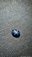 Natural blue star sapphire oval cabochon on a textured dark background showing 6-ray star effect under lighting.