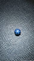 Close-up photo of natural round cabochon sapphire showing the star effect on a textured background.