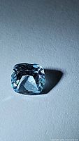 Close-up photo of a natural cushion cut sky blue topaz gemstone, approximately 6mm in size, showing clarity and faceting details.