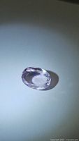 Oval cut pink-purple amethyst gemstone photographed on white background under light showing clarity and cut.