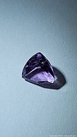 Purple trillion cut amethyst gemstone on blue background with visible facets and clarity details.