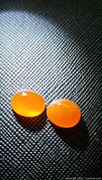 Two oval mandarin orange carnelian cabochon gemstones on a textured black background, showing smooth polished surfaces and vibrant color.