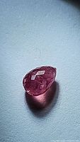 Close-up image of the natural pink-red ruby with briolette cut showcasing facets and internal inclusions.