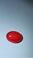 Clear photo of deep fire red orange oval cabochon fire opal gemstone on white background showing color and smooth polished surface.