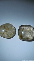 Two natural golden rutilated quartz stones laid side by side on a white surface showing internal golden rutile inclusions