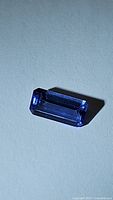 Close-up image of the octagon cut deep purple blue tanzanite gemstone resting on a plain surface with visible facets and clarity.