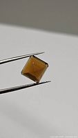 Close-up photo of the natural Madeira citrine gemstone held by tweezers showing its faceted square cut and cognac color.