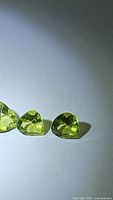 Three pear-cut natural peridot stones, light green, faceted, shown on white background from an angle to highlight clarity and color.