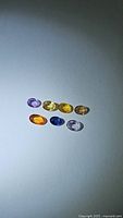 Top-down view of seven natural oval cut sapphires in different colors on white background.