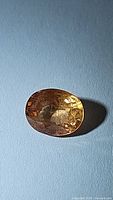 Oval cut mandarin orange yellow sapphire gemstone placed on a blue background showing clarity and color.