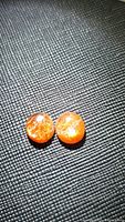 Two round cabochon cut sunstone gemstones with orange color and bright flash, placed on textured black surface.