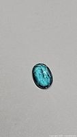 Close-up photo of blue oval polished topaz gemstone on grey background.