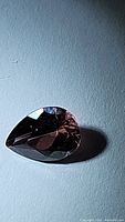 Close-up image of the pear-shaped tourmaline gemstone showing its dark rich purple shades with facets visible.
