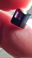 Close-up photo of deep purple octagon cut tourmaline showing the gem's color, cut edges, and internal clarity held between fingers.