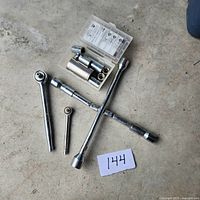 Full view of all tools including 4-way lug wrench, small ratchet wrench, and socket wrenches laid on the floor alongside the container with nuts.